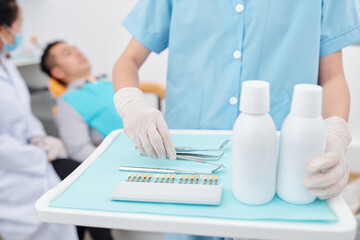 Cropped of assistant preparing tray for dentist and putting tools, teeth color palette and bottles of antiseptic mouthwash product