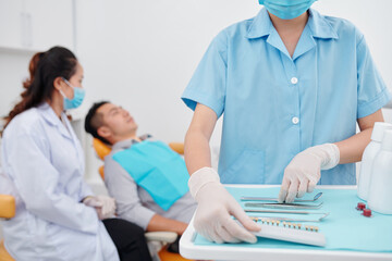 Assistant in latex gloves preparing tools for dentist who is talking to patient in background