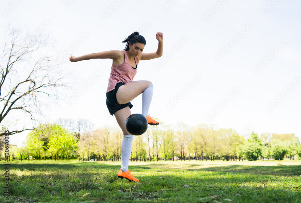 Wall mural Young female soccer player practicing on field.