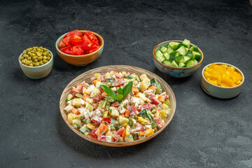side view of bowl of vegetable salad in the center with bowls of vegetables on side on dark grey background