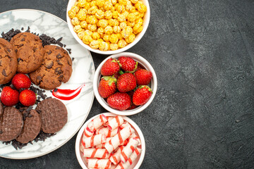 top view delicious various biscuits with a bowl of ripe strawberries cookies on a black surafce with free space