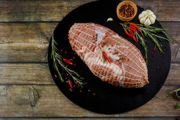 Raw fresh pork shoulder with spices on black wooden board.