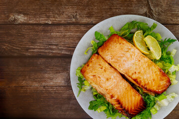 Cooked salmon fillet in plate on wooden background.