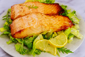 Close up of cooked salmon fillet with lemon in plate.