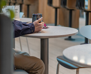 men hands holding a cup of tea or coffee mug sitting in cafeteria.