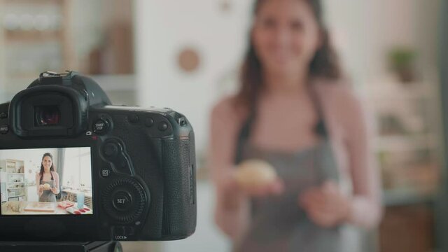 Blurred Caucasian female blogger making dough balls, putting them in silicone baking form, showing them on camera in front of her, recording process, video playing on its screen