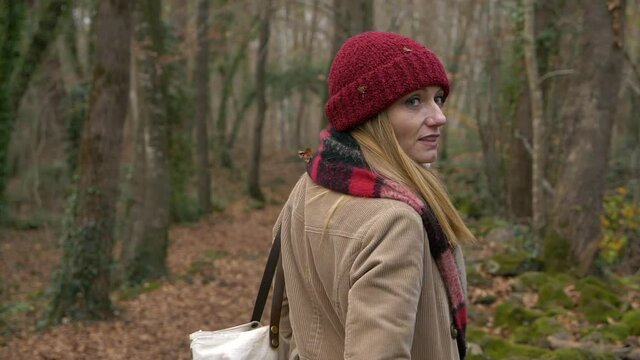 Woman in red hat turns to smile at camera while walking in autumn forest, Slowmo