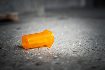 A close up of an empty plastic orange colored pill container or vial with no lid or cap from a pharmacy laying littering the sidewalk in downtown Chicago.