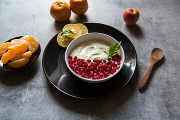 Close up of pomegranate seeds on curd along with fresh fruit ingredients of apples and oranges on a black plate.
