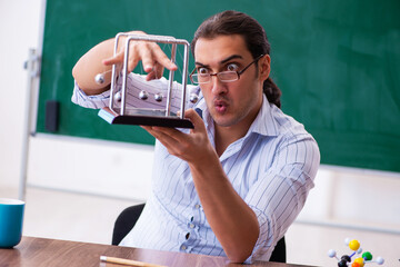 Young male teacher physicist in front of blackboard