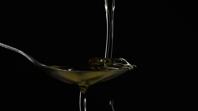 Close-up pouring olive oil liquid into spoon on black background in slow motion