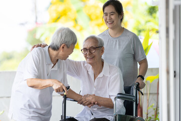 Happy asian elderly woman sit in wheelchair with female caregiver,senior grandmother greeting and welcoming visiting friend or her family embracing enjoy at front door during Christmas holiday at home