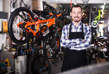 Young positive man working as mechanic for assembly of bicycles in store workroom