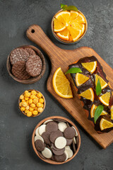 Vertical view of tasty cakes cut lemons with biscuits on cutting board on dark table