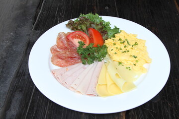 Breakfast, scrambled egg, cold cuts Swiss cheese, salami and salad garnish