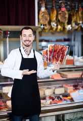 attractive man seller showing sliced bacon in butcher shop