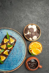 Vertical view of delicious cake decorated with lemon and chocolate with other cookies on dark table