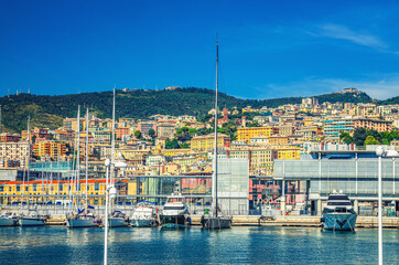 Port Porto Antico harbor with luxury white yachts in historical centre of old city Genoa Genova with blue sky in clear summer day and green hill with residential buildings background, Liguria, Italy