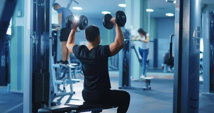 Sportsman bodybuilder trainer working out weightlifting heavy black dumbbells alone in professional gym blue interior. Strong man. Active sports.
