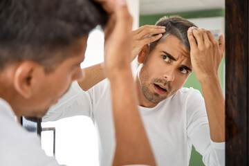 Stressed man with graying hair looking in mirror