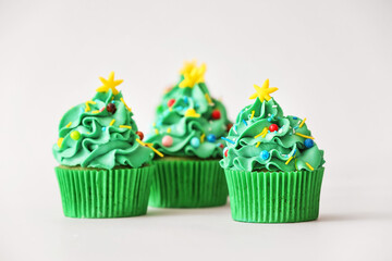 Tasty Christmas cupcakes on light background
