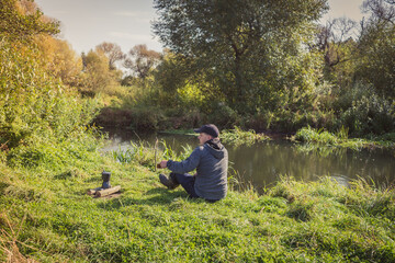 Man sitting near a fire on the river bank. Rest at nature. Man sits alone on the bank of the river near the fire.