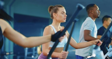 Multi-ethnic group of fitness athletes with female instructor exercising on cross trainers treadmill in the modern gym together. Sports team.
