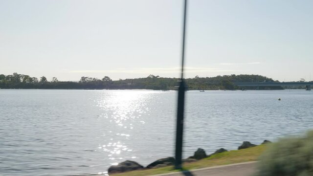 Journey along beautiful Canning River with trees in background. Tree-lined path in foreground. Approaching large bridge. Rowing activity seen