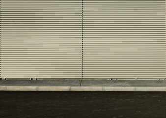 Beige aluminum striped cladding wall, with a concrete sidewalk and a asphalt street in front....