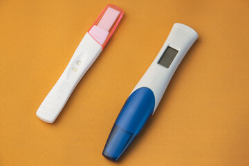 Two pregnancy tests, digital and analog, lie on a yellow background