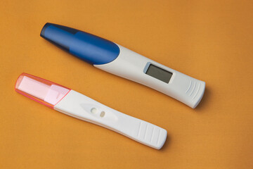 Two pregnancy tests, digital and regular, lie on a yellow background
