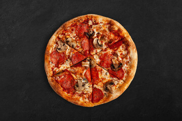 Tasty pizza with salame and mushrooms on dark concrete surface. Top view of sliced pizza. 