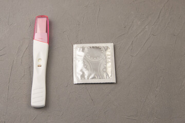 A negative pregnancy test and a condom on a gray concrete background. The concept of preventing unwanted pregnancy