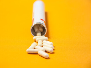 A bottle with scattered pills on a yellow background. Selective focus