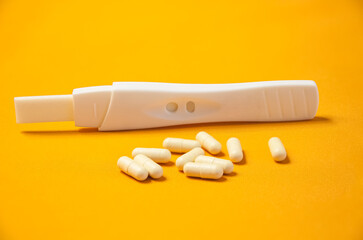 A pregnancy test and a handful of birth control pills on a yellow background