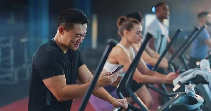 Asian handsome young positive man chatting messages using smartphone recording voice audio message while workingout with team sports in modern gym.