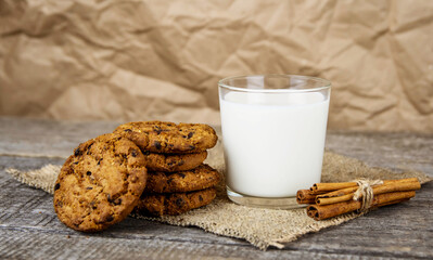 A glass with milk and oatmeal cookies, cinnamon sticks on burlap on a wooden background.