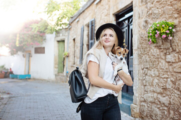 Fototapeta na wymiar Lifestyle image of happy young woman walking old city street with small jack russell dog.Drinking tea. Wearing stylish minimalistic outfit. Freedom and happiness concept. Tourism and adventure