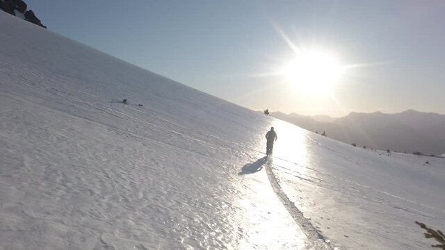 Dolly in following a man skiing alone across snow covered Piltriquitron Hill at sunset, El Bols&oacute;n, Patagonia Argentina.