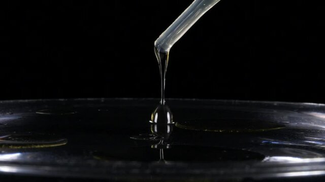 Pipette dropper pours oil in water on black background, Slow Motion Closeup