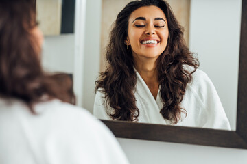 Happy woman with closed eyes standing in front of a mirror in bathroom