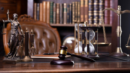 Fototapeta na wymiar Law and justice theme. Judge chamber. Themis statue, gavel and scale on brown desk. Legal books in the bookshelf as background.