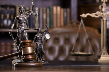 Law and justice theme. Judge chamber. Themis statue, gavel and scale on brown desk. Legal books in the bookshelf as background.