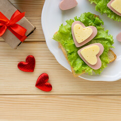 Breakfast for valentine's day. Sandwich with sausage, cheese and lettuce on white plate