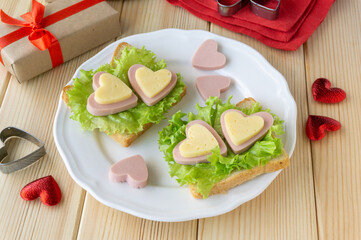 Breakfast for valentine's day. Sandwich with sausage, cheese and lettuce on white plate
