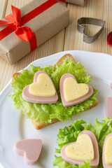 Breakfast for valentine's day. Sandwich with sausage, cheese and lettuce on white plate