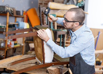 Qualified workman upholstering chair in repair furniture workshop