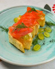 Traditional salmon puff pastry with fresh grapes. Delicious recipe. Served on a plate over traditional tablecloth.
