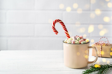Christmas or New Year composition. Mug of hot chocolate or cocoa with candy cane and marshmallow on white wooden table. Festive, winter, cosy holidays concept.