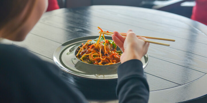Beautiful young woman eating chinese food called Wok with chopsticks. Wok with meat and fried asparagus in a plate.